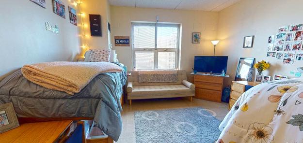 A bright residence hall room with a couch, desk, tv and bed.